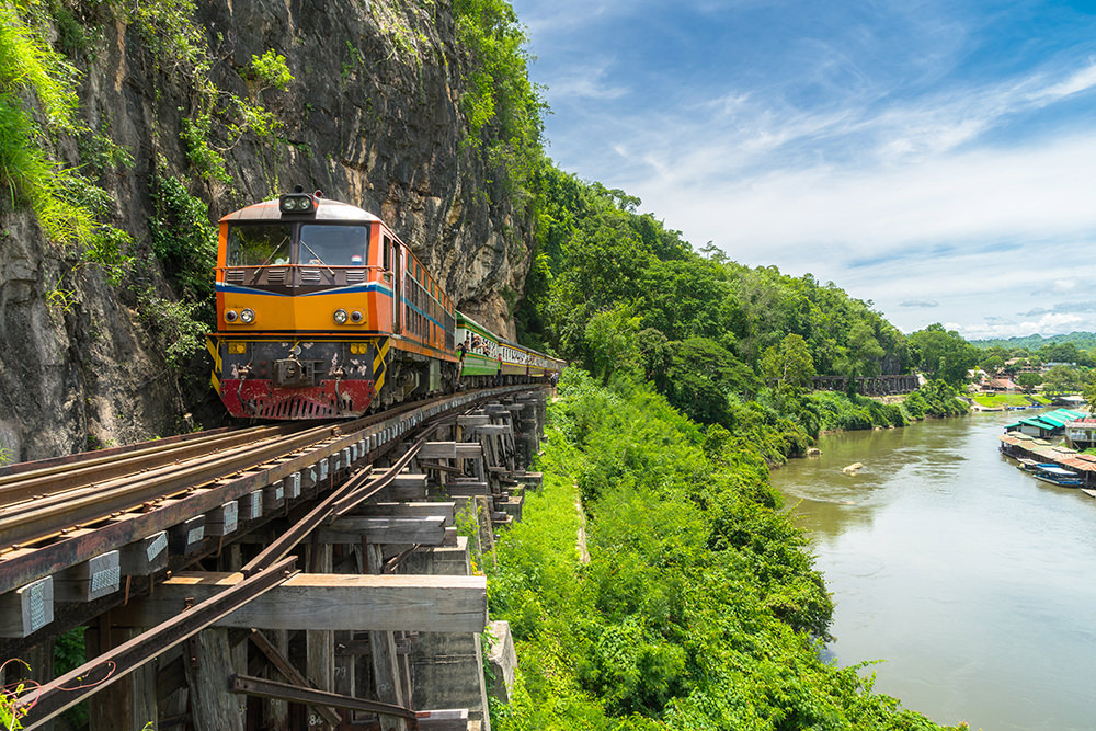 The railway train on the side of a big rock and by a river in Kanchanaburi, Thailand.