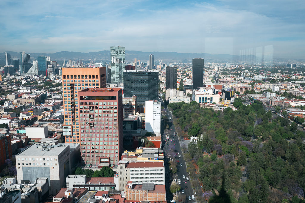 A high-angle view across Mexico City, showcasing buildings, Paseo de la Reforma, and a green space with a winding road