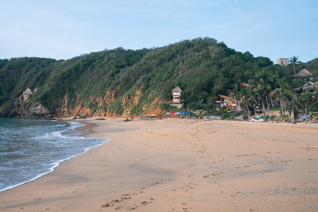 Mazunte beach with a large, lush green hill rising steeply from one side of the beach, in Oaxaca, Mexico