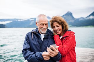 A middle-aged couple happily looks at a phone near a body of water.