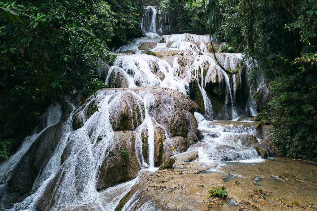 Multi-tiered Air Terjun Saluopa waterfall cascading over rocks surrounded by lush green vegetation